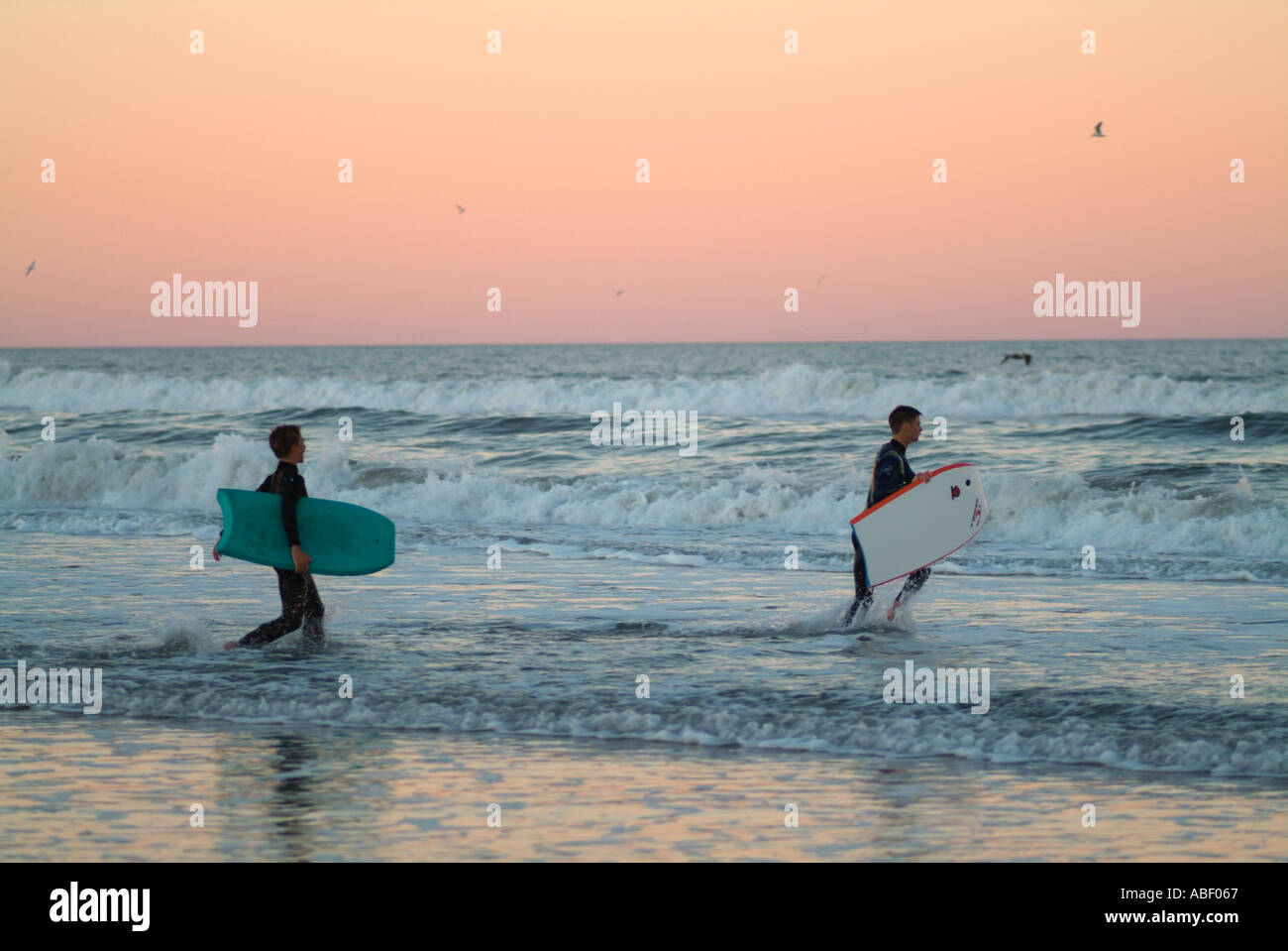 Boys with boogie boards head into the surf dusk sky Stock Photo