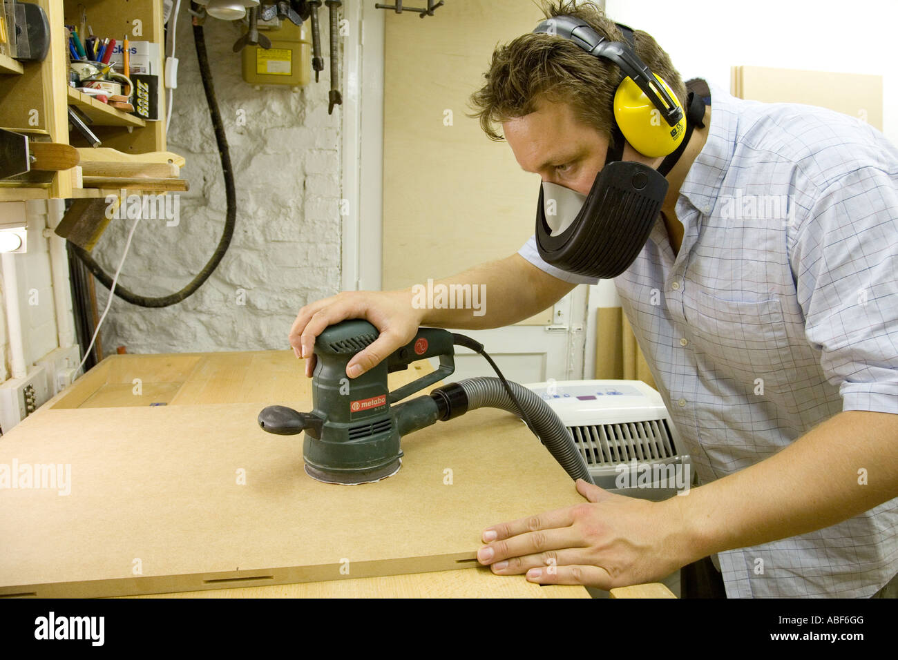 A craftsman uses a random orbit sander with dust extraction to finish a piece of MDF prior to