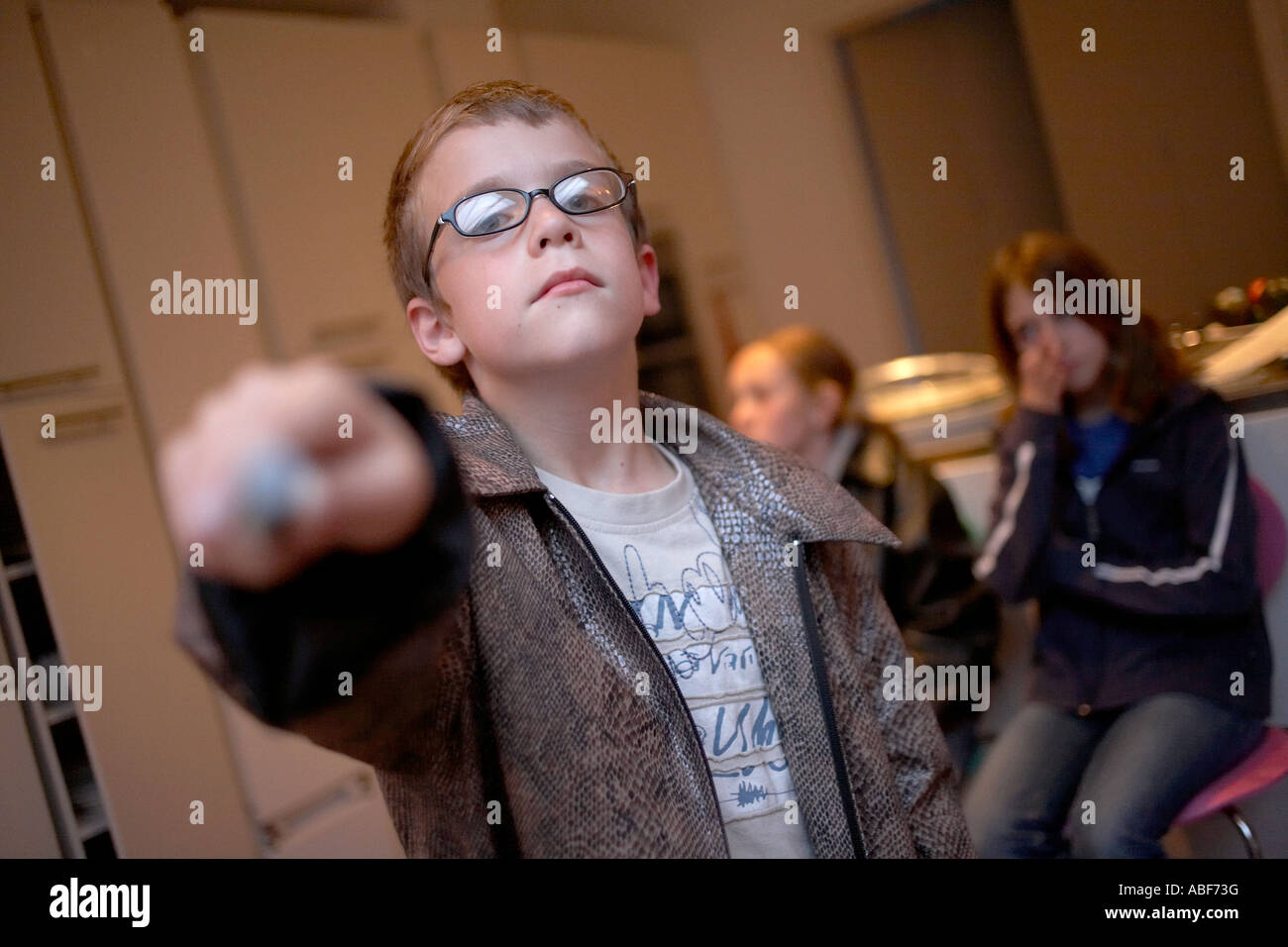 A nine year-old English boy wearing glasses waves a magic wand while playing a Harry Potter game with friends. Stock Photo