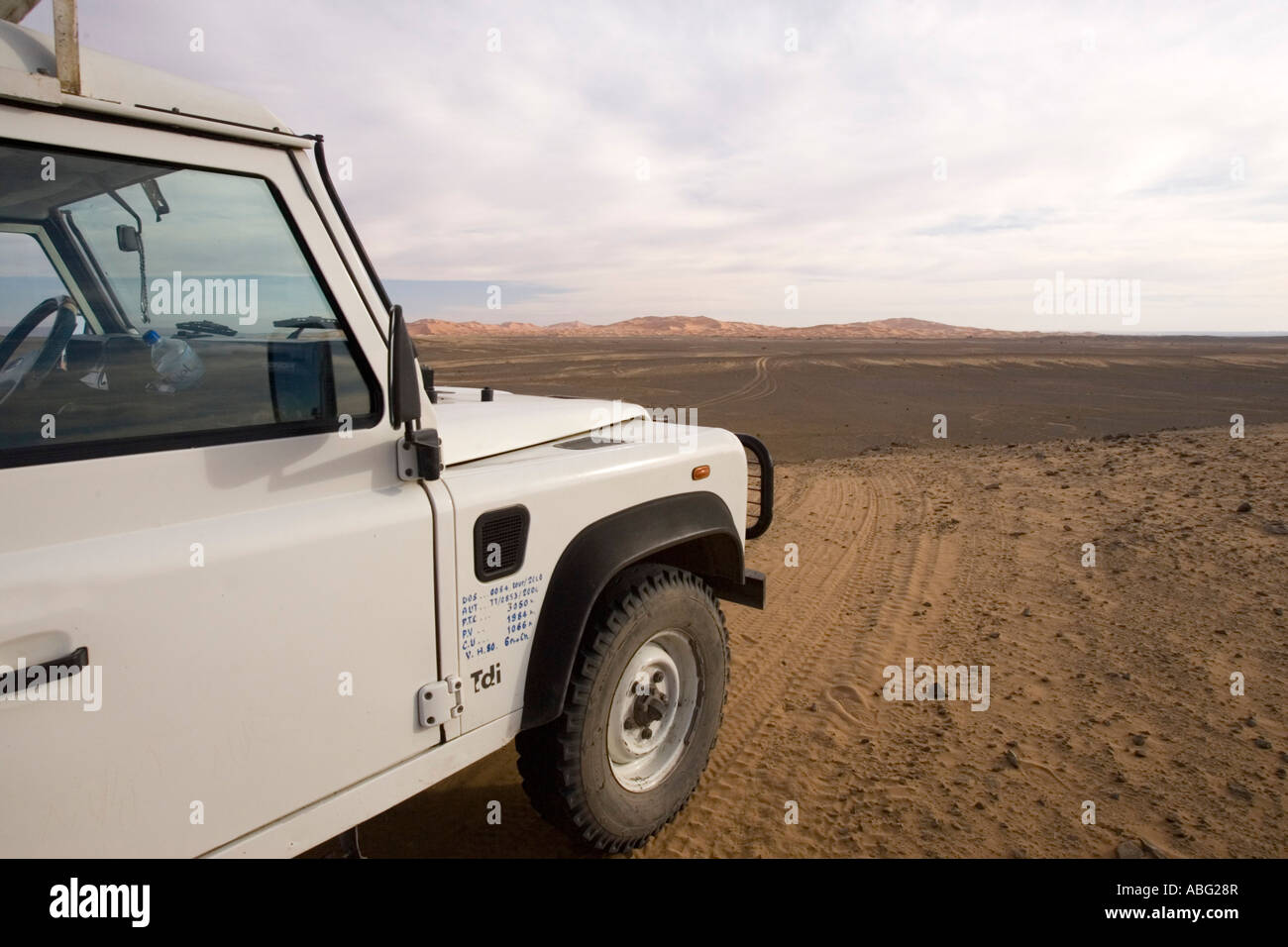 Land Rover Defender four wheel drive vehicle on piste track approaches large sand dunes at Erg