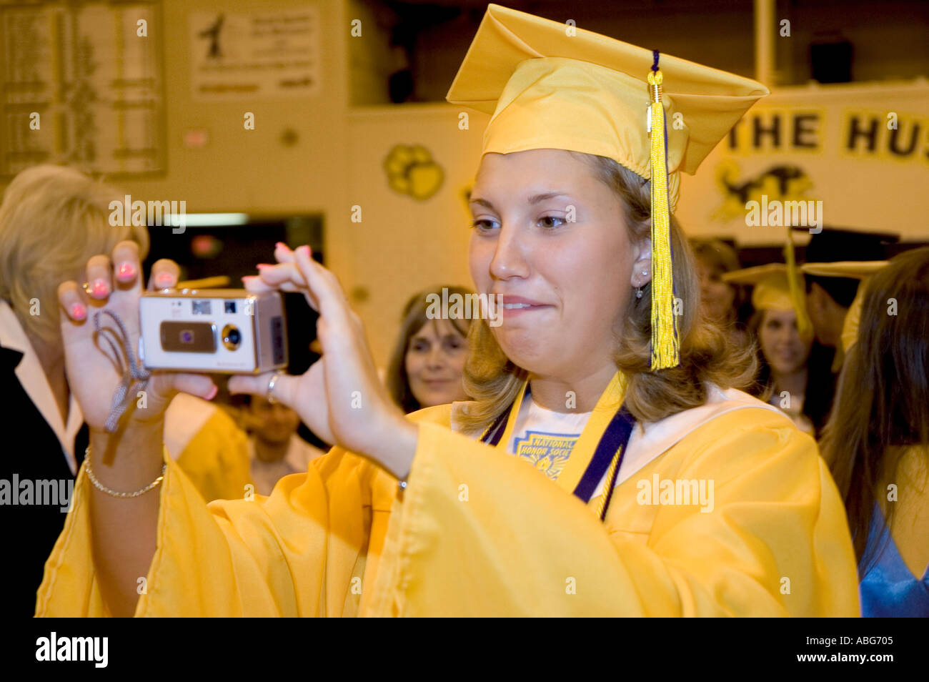 Senior in yellow cap and gown looks at the back of a digital camera
