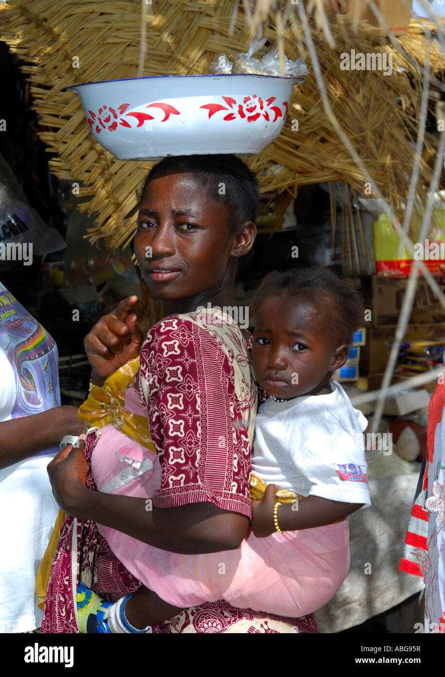 Young woman with toddler on the back balancing a bowl on her head, Burkina Faso Stock Photo