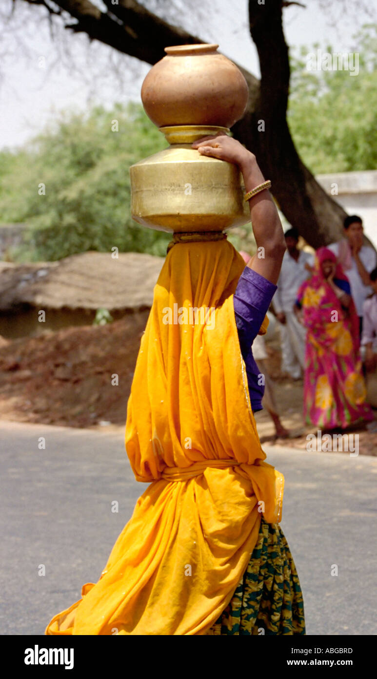Woman carrying pots on head after filling them from the local village