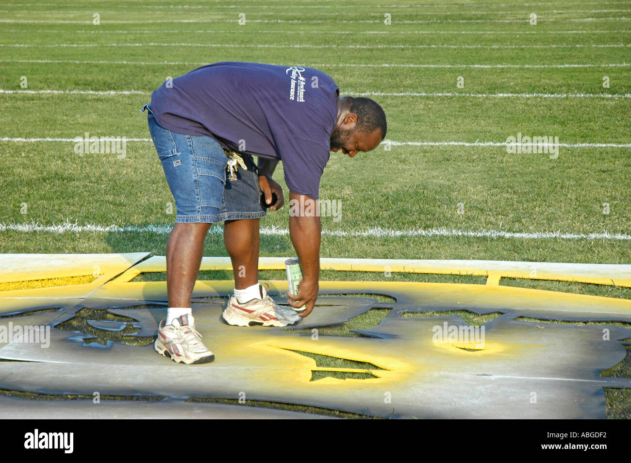 Ethnic father who is black is painting yardage numbers and logos on football fields in