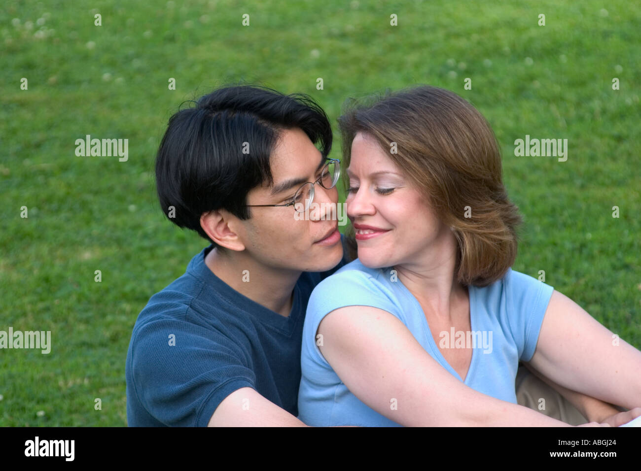 Interracial couple sitting on a lawn in a park Stock Photo