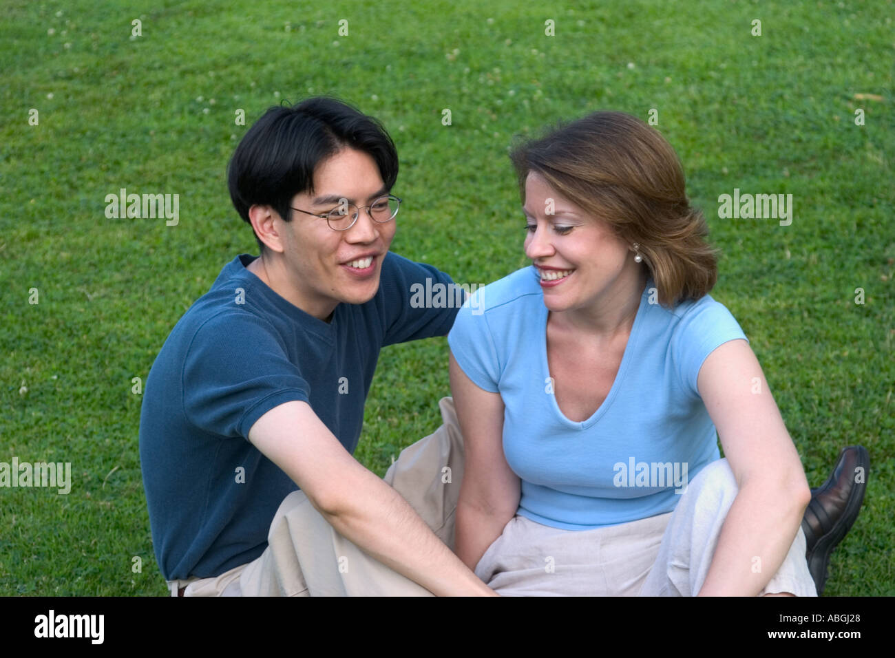 Interracial couple sitting on a lawn in a park Stock Photo