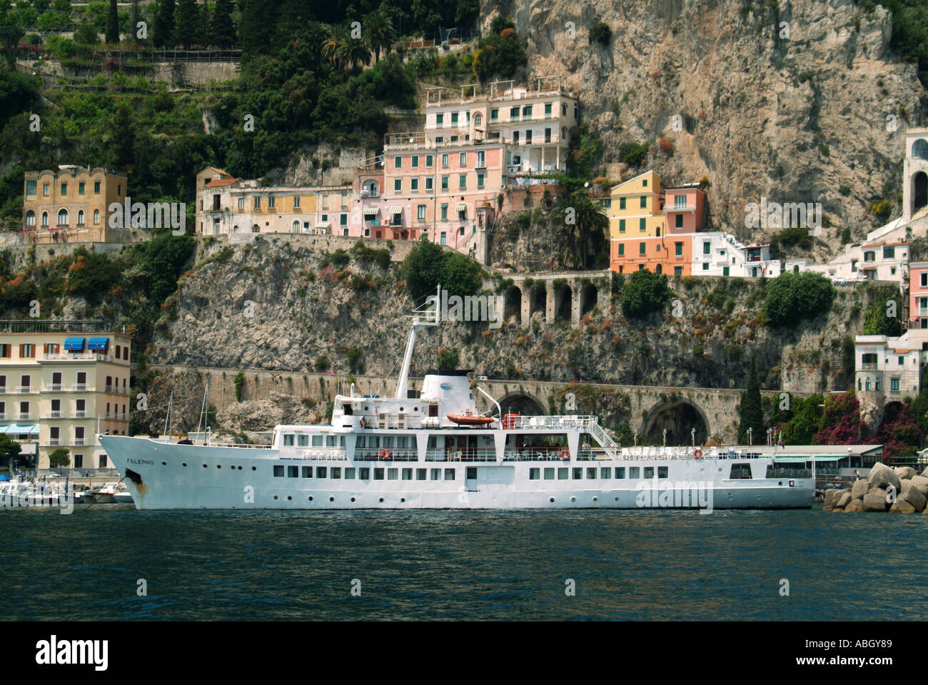 Amalfi town waterfront anchored sightseeing tour boat named Falerno in front of UNESCO coastline & cliff face buildings at Salerno Campania Italy EU Stock Photo