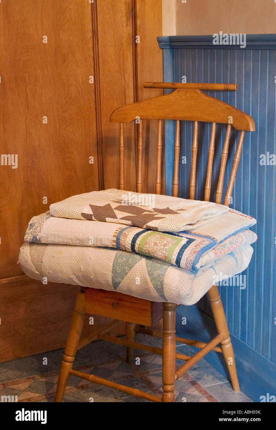 Folded quilts on a wood chair with blue wainscoting behind. Stock Photo