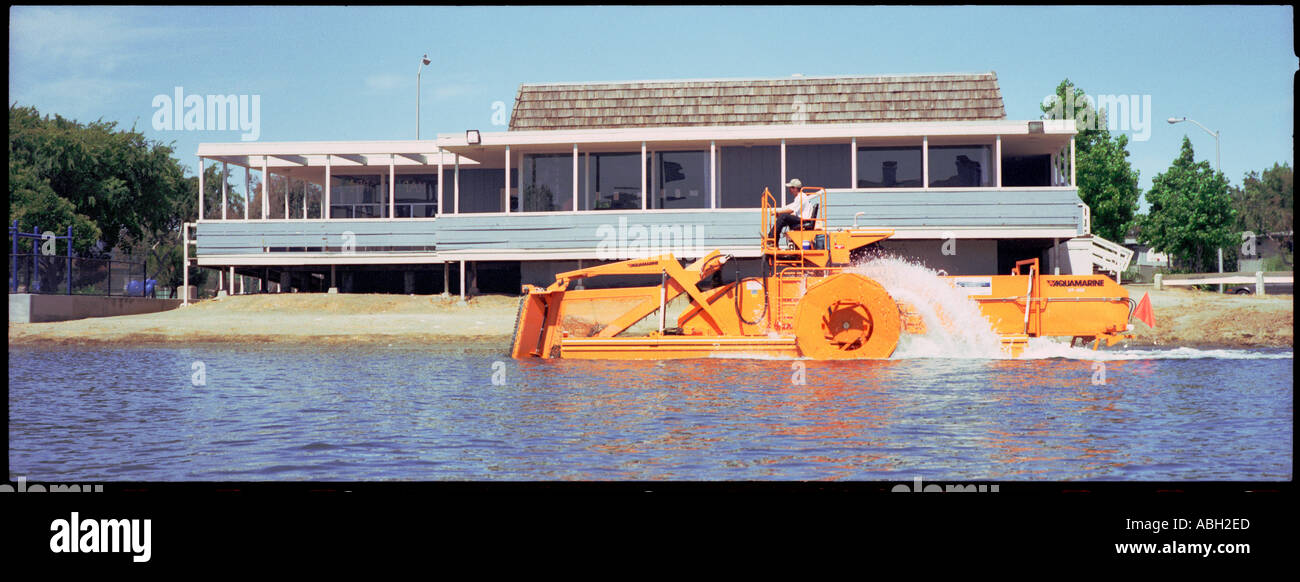 A man on a big bright yellow dredger clearing a lagoon Stock Photo