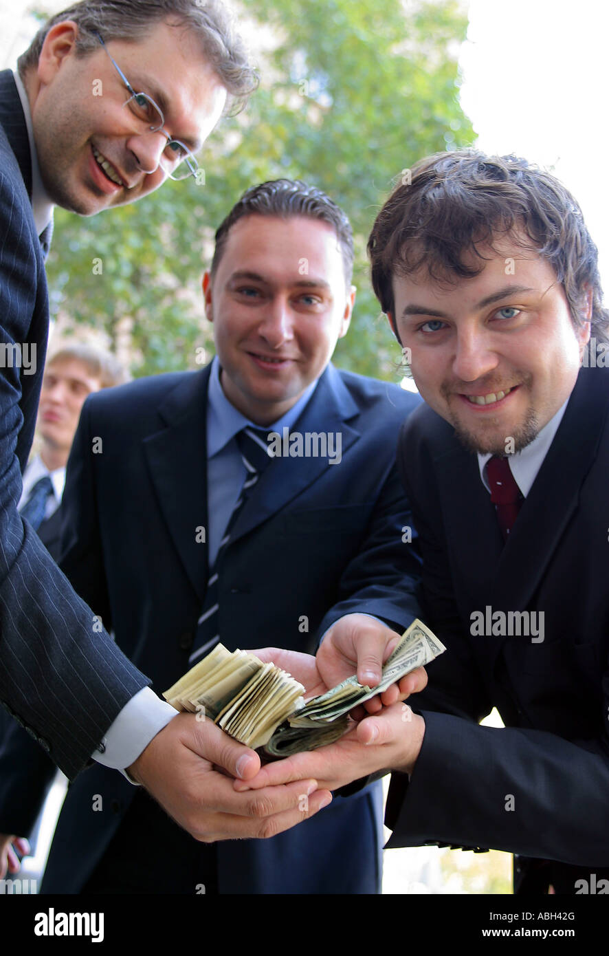 A portrait of three businessmen in suits seen here holding a large amount of dollar bills. Stock Photo