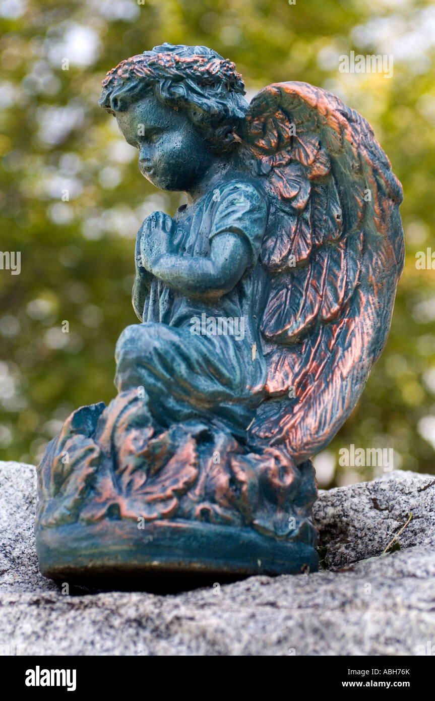 A praying angel statue in a cemetery on top of a gravestone Stock Photo