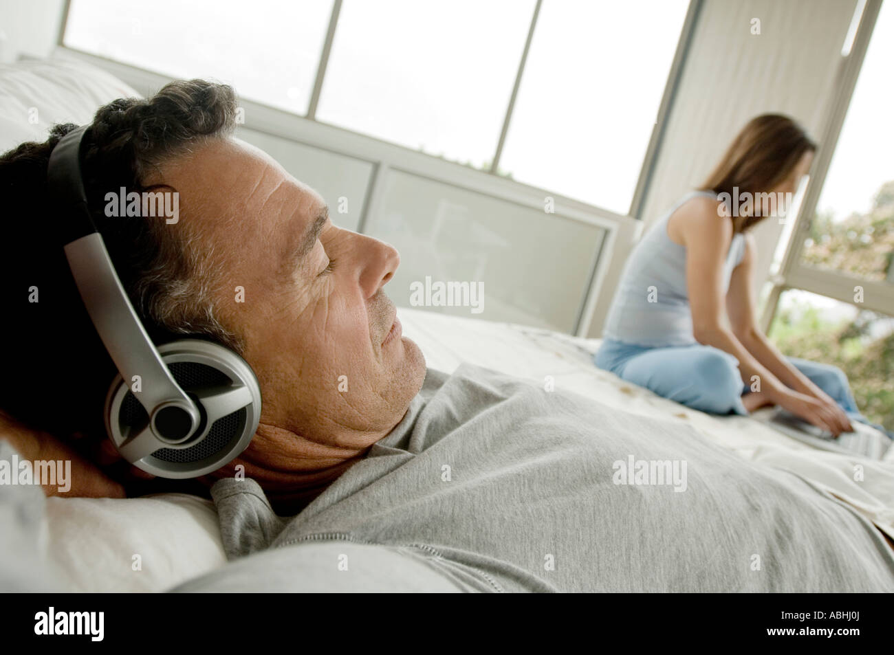 Man lying on bed, listening to music with headphones, woman in ...