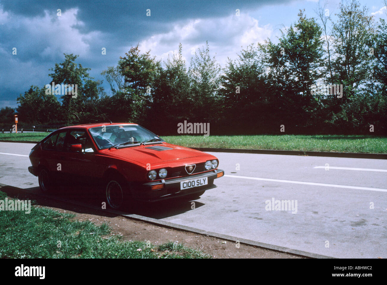 Red Alfa Romeo GTV6 coupe parked in a layby with a stormy sky Stock Photo