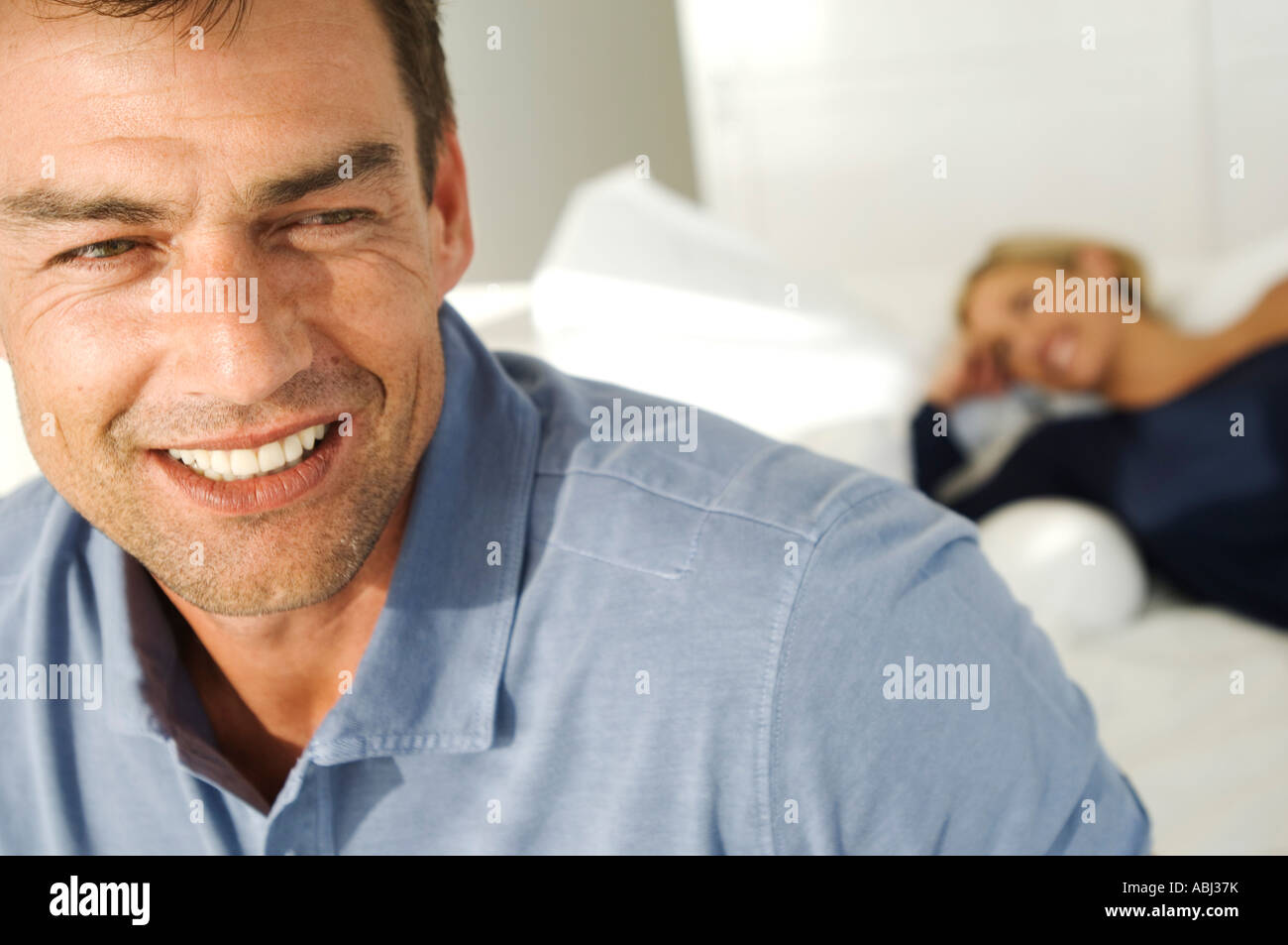 Portrait of smiling man, woman lying on bed in background Stock Photo ...