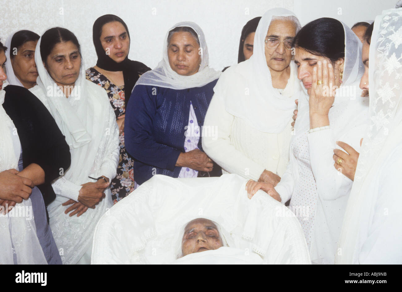 Sikh women pay their final respects to a relative lying in state in her coffin, 1980s Stock Photo