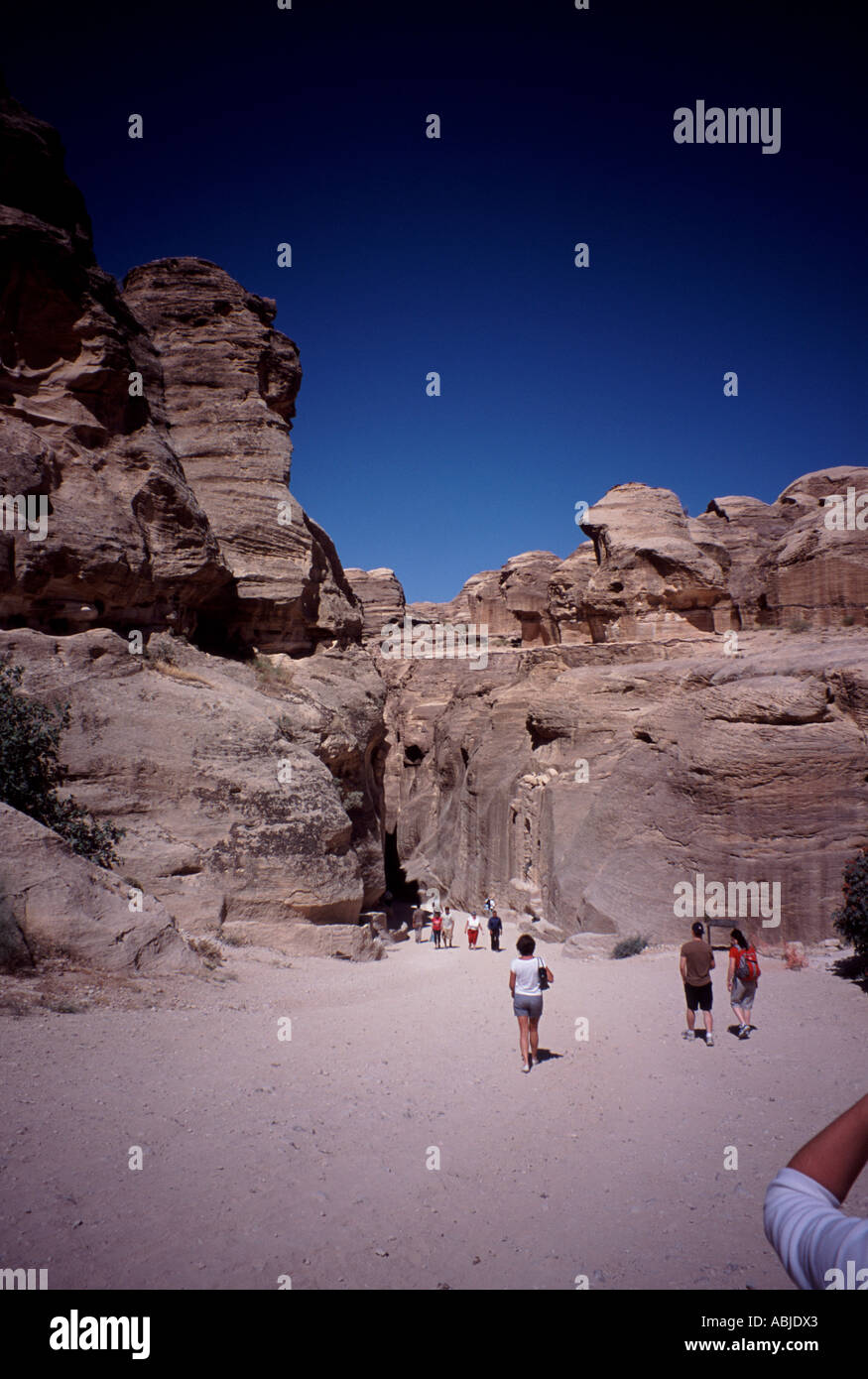 Tourists dwarfed by wind eroded rock buildings in Petra, Jordan Stock Photo