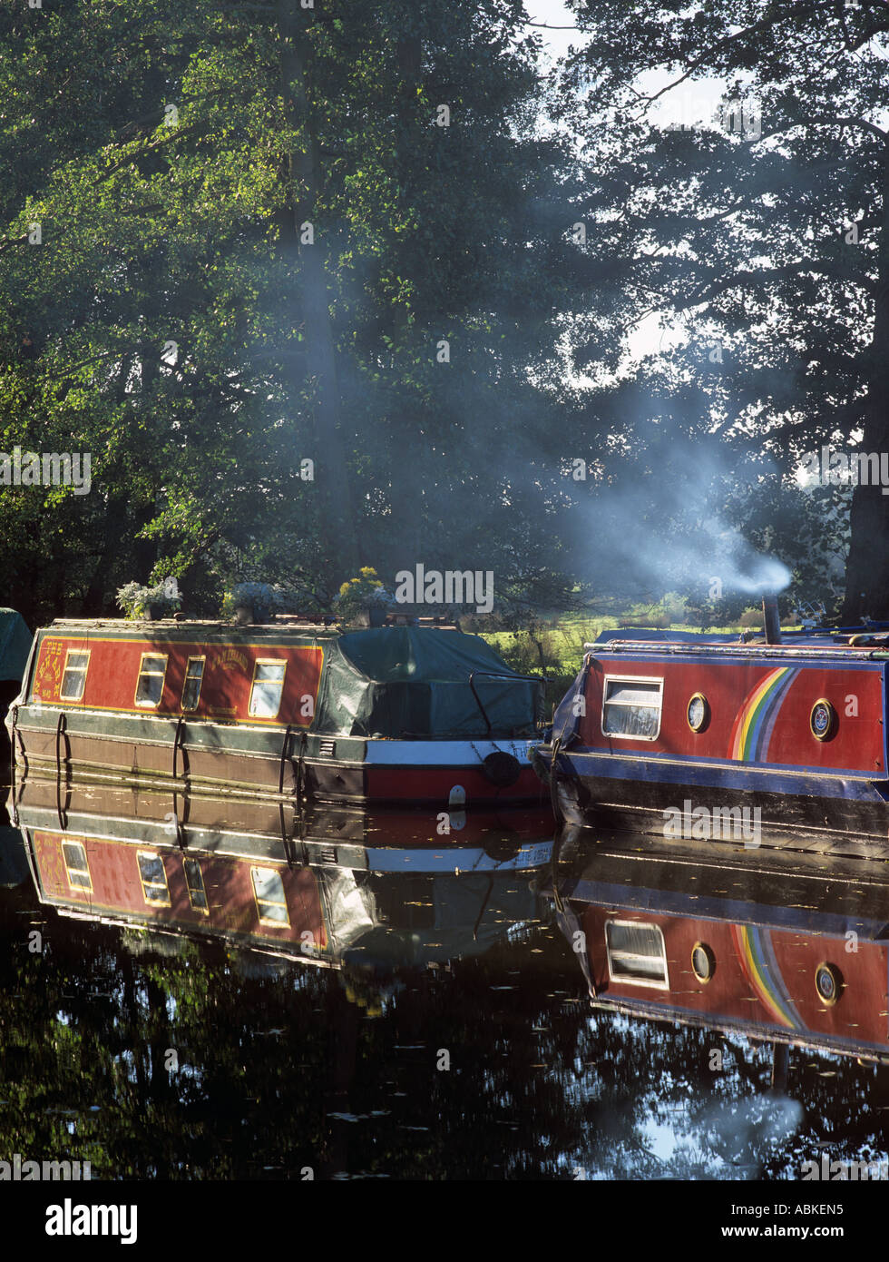 Moored canal narrow boats on Wey Navigation with smoke rising on cold winter early morning Sutton Green Surrey England UK Stock Photo