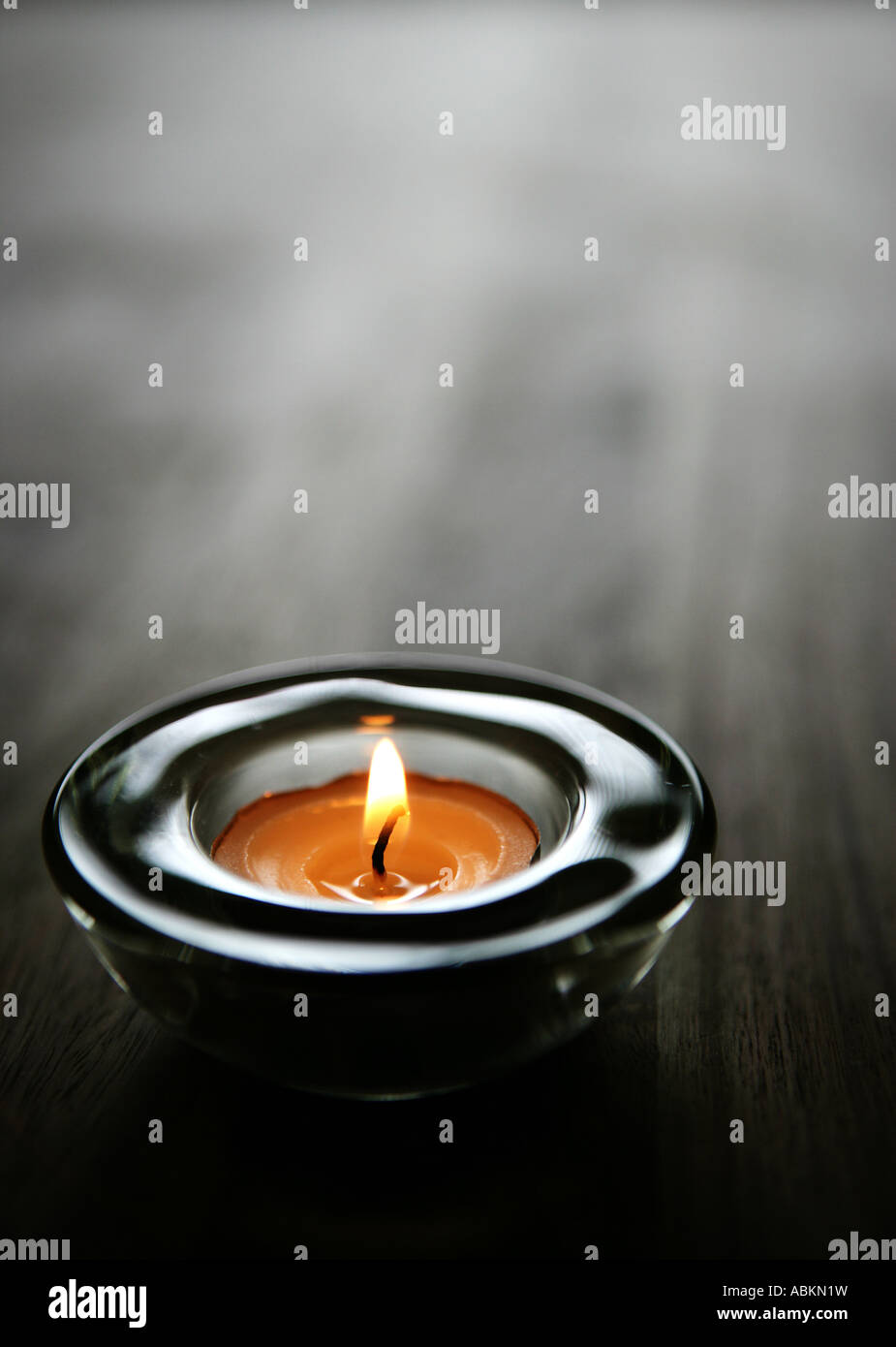 A single decorative tea light candle on a natural wood coffee table top