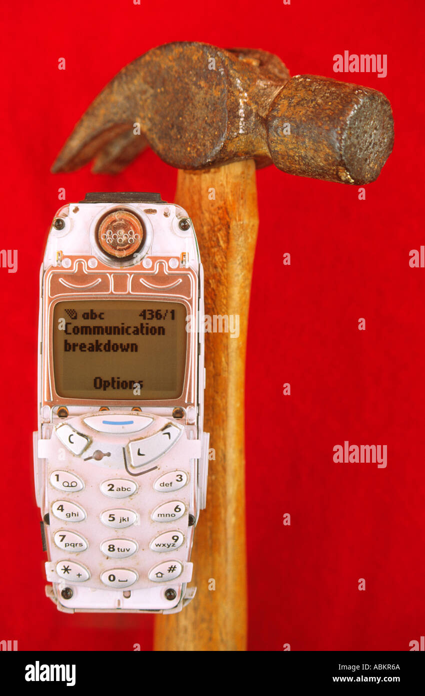 Still life theme of a broken mobile phone about to be hit with a hammer The screen reads COMMUNICATION BREAKDOWN Stock Photo