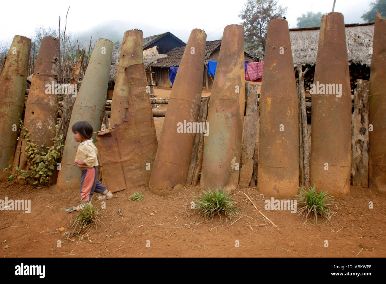 A child walks past a fence made from bomb casings. Northern Laos Stock Photo