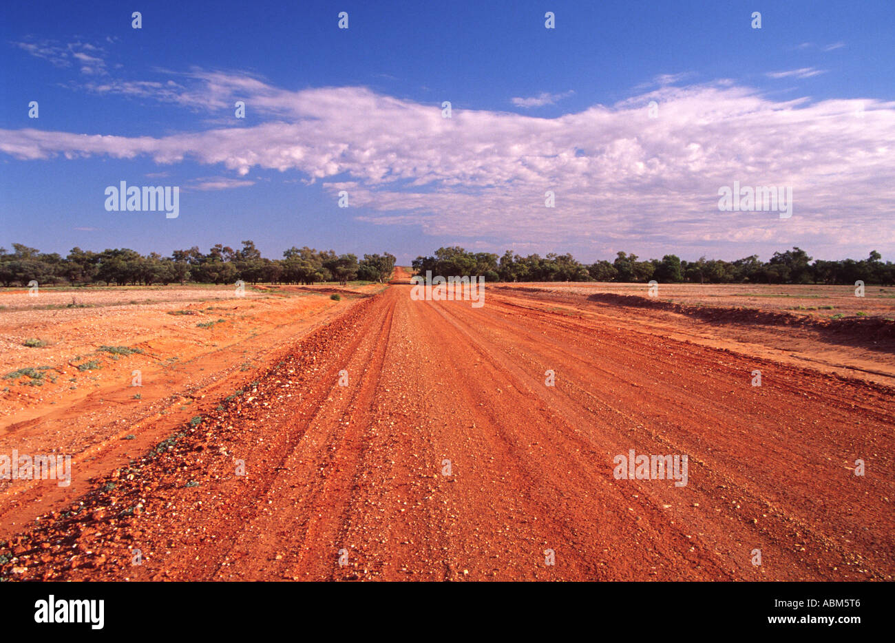 A long red dirt road in the Australian outback stretches across vast red plains to the distant