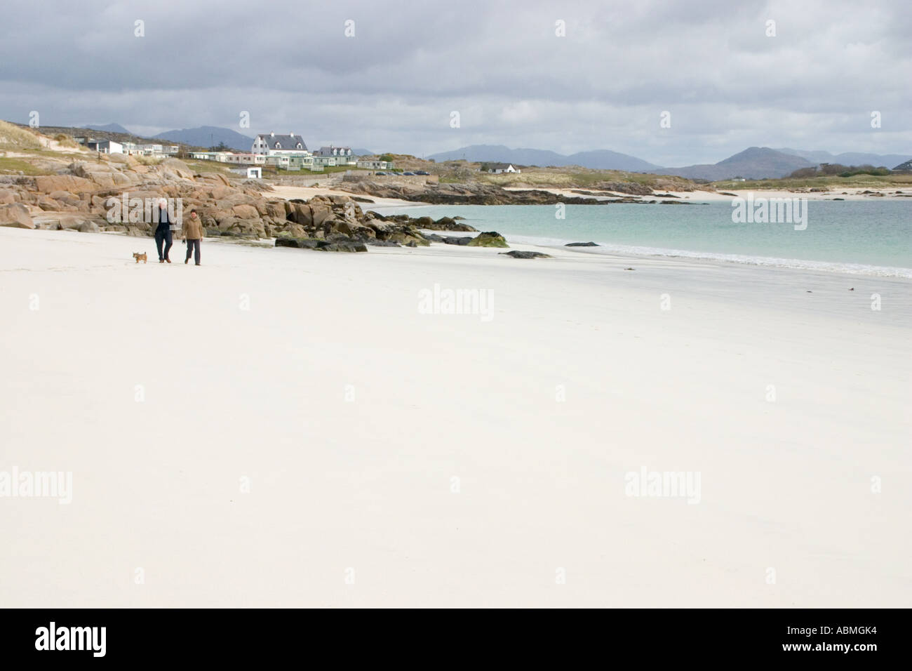 Couple and dog walking on white sands of Gurteen Bay Connemara Ireland Stock Photo