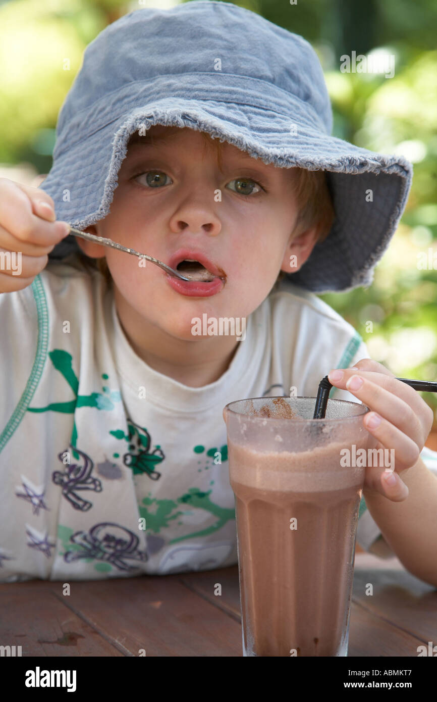 young child in summer wearing floppy sun hat at a cafe having a large glass of iced chocolate Stock Photo
