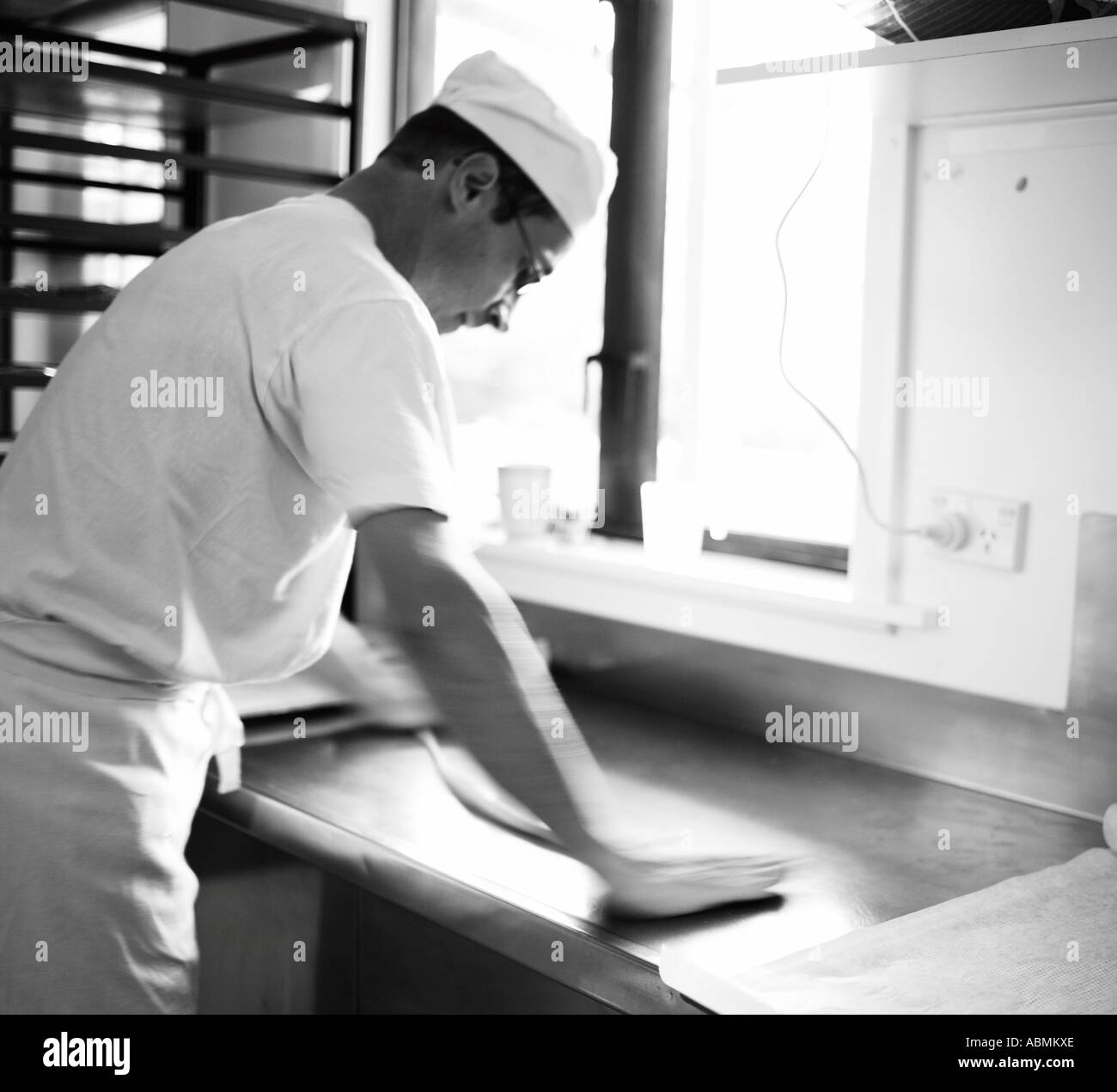 male baker in the bakery baking bread brezels in small commercial kitchen rolling out before putting them on baking trays Stock Photo