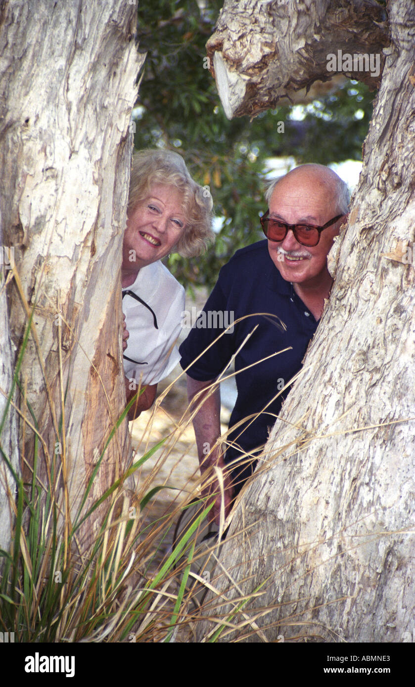 beautiful happy retired couple playing peekaboo from behind gum tree at Boreen Point Sunshine Coast Australia Stock Photo