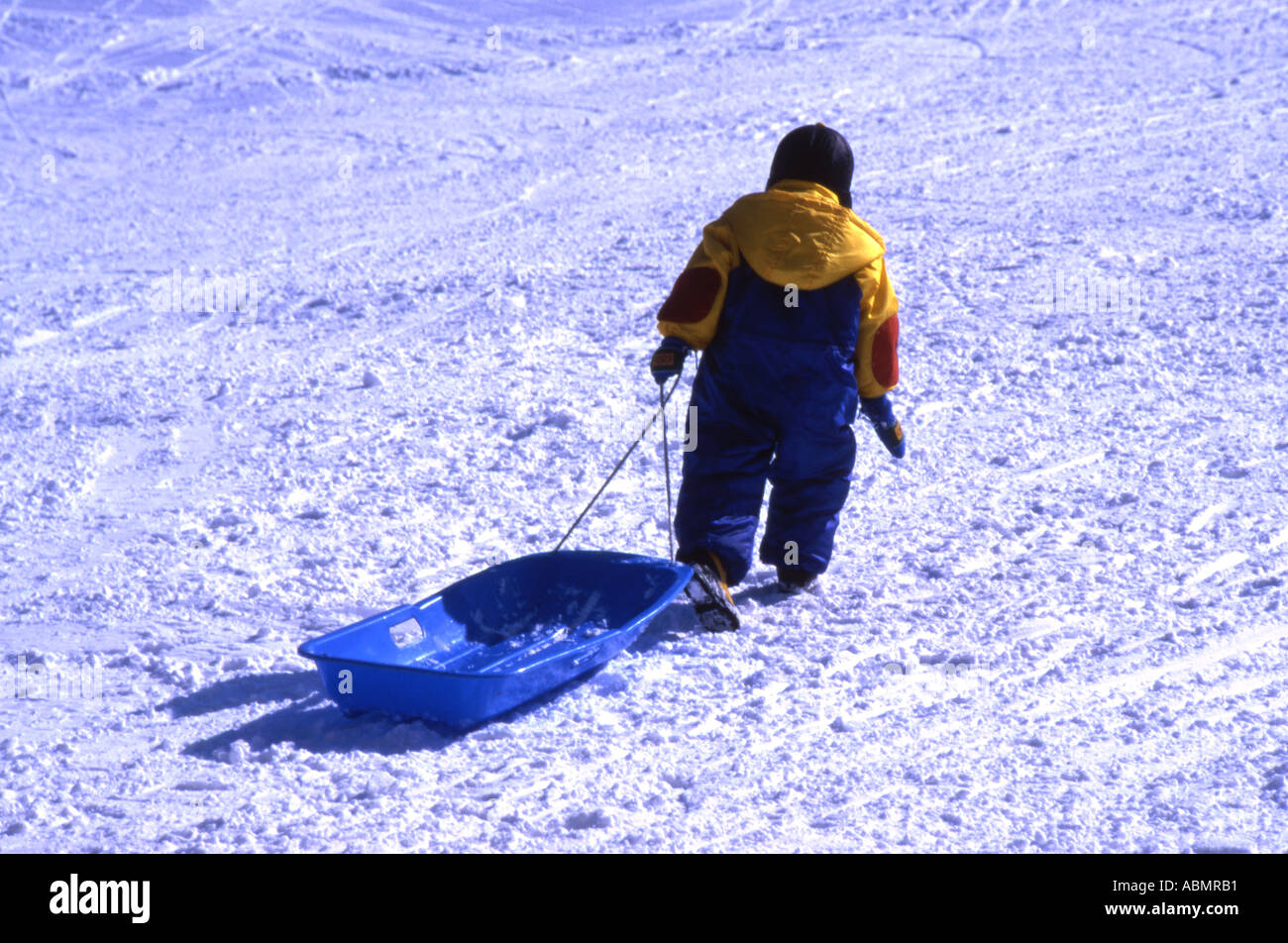 Young boy climbs back up the snow covered slope with his sled Stock Photo