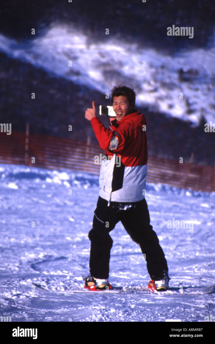 Young Japanese man with video camera slides down the slopes on his snowboard Stock Photo