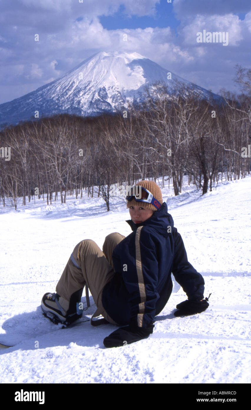 Japanese snowboarder girl sits on the snow with Mt Yotei in the background Stock Photo