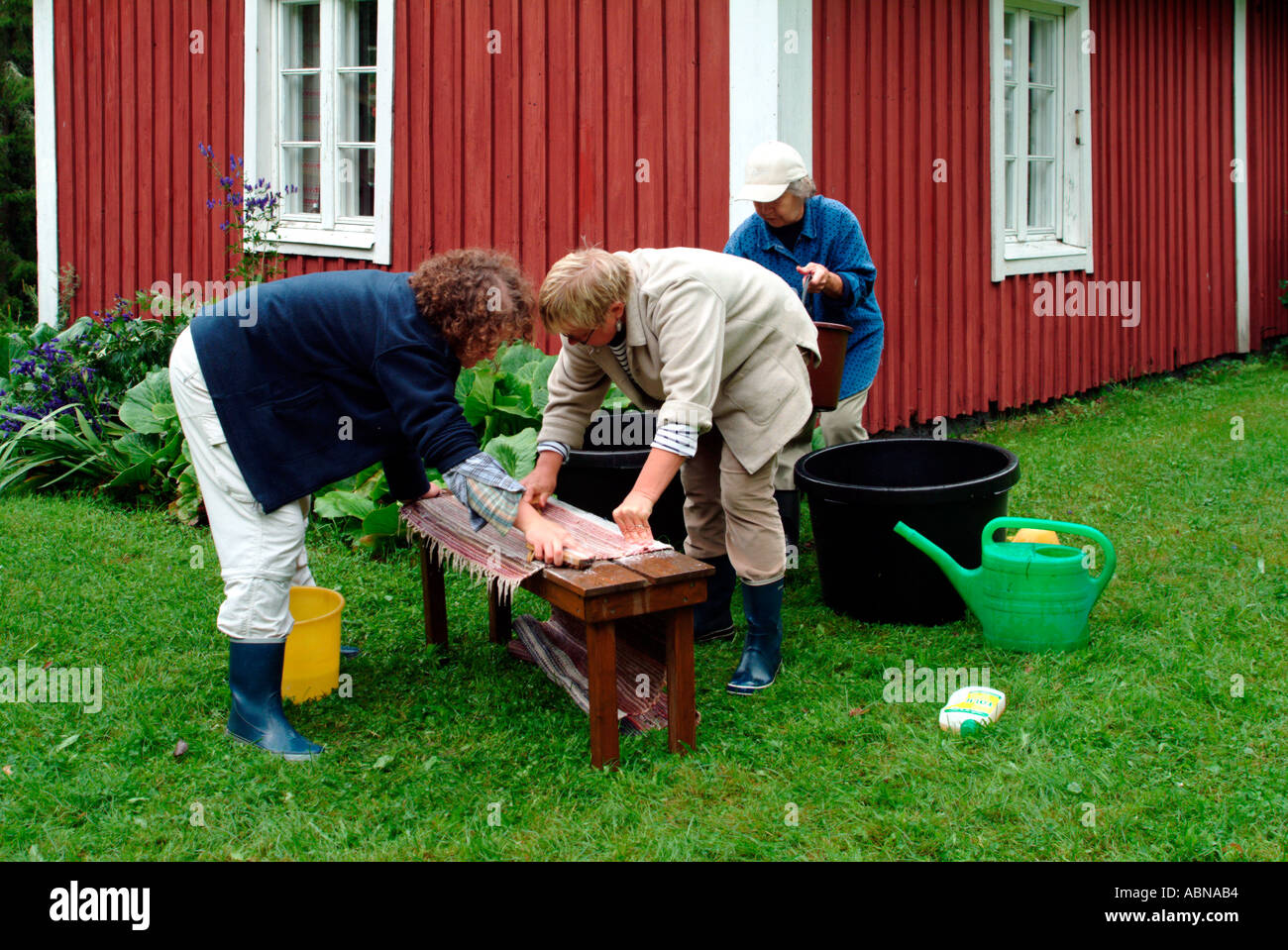 three generations of women cleaning rag rugs in front of a wooden red