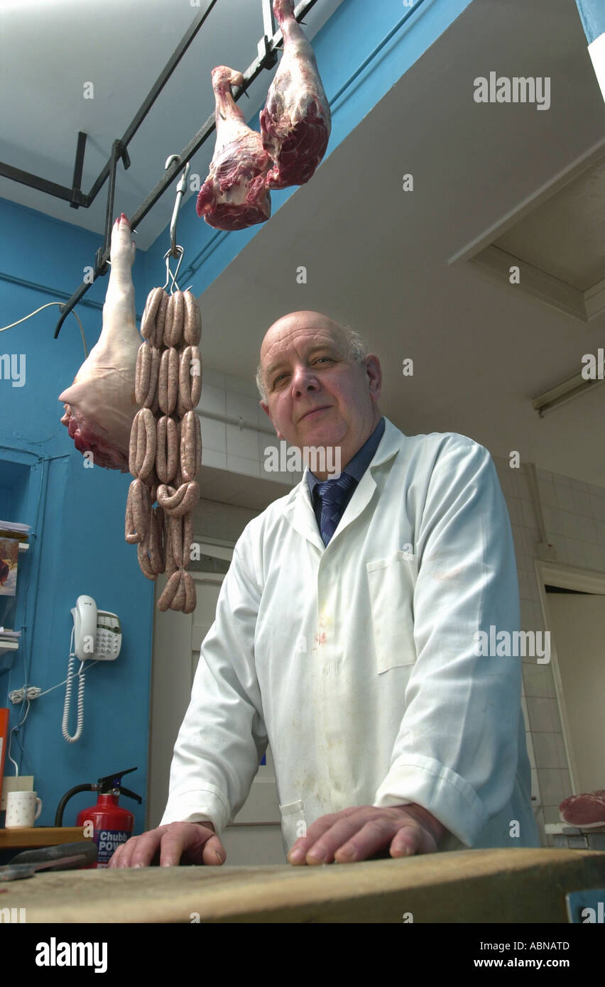 Butcher holds a string of sausages hanging from a hook in his shop UK Stock Photo