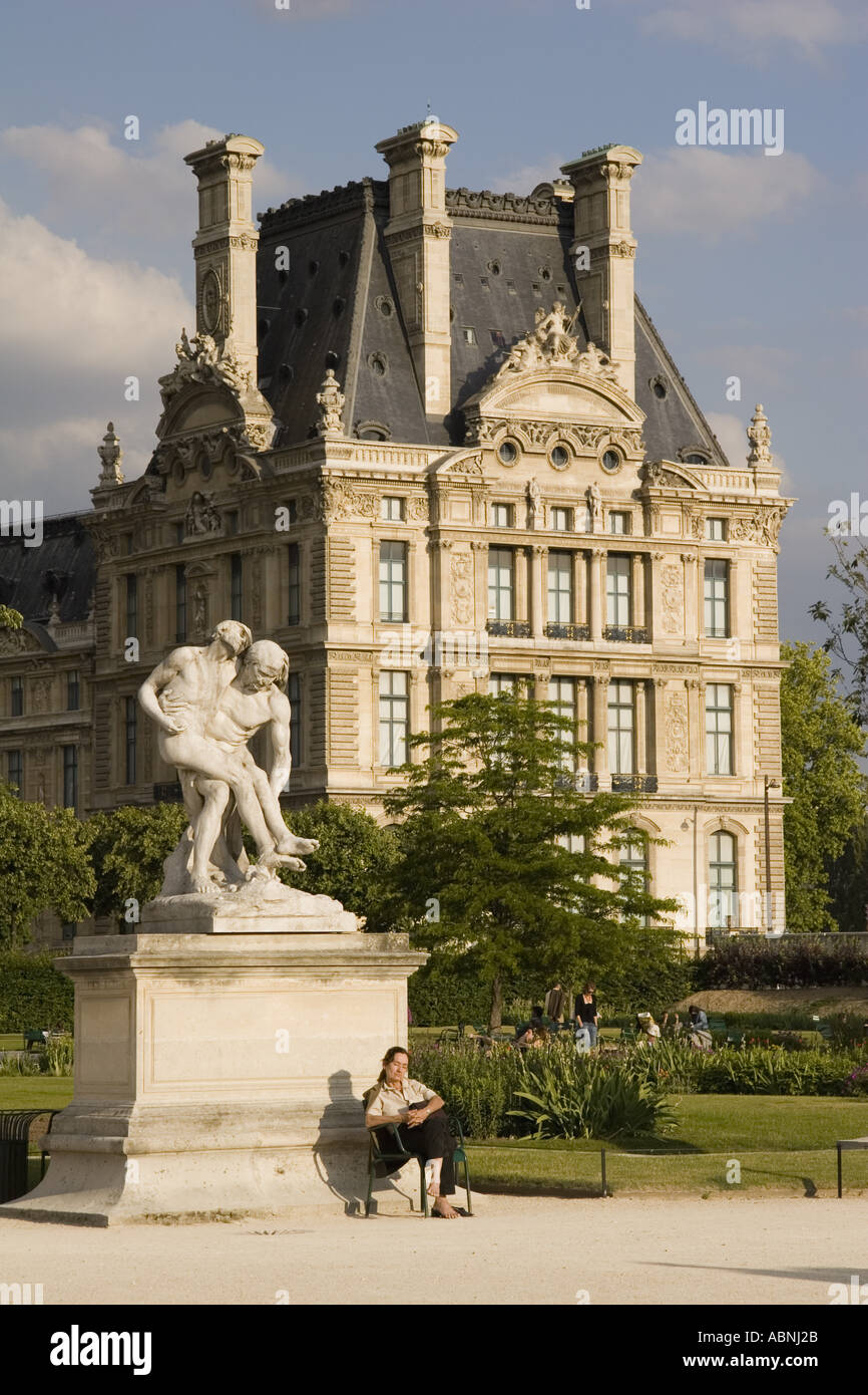 Woman sits in late afternoon sunshine in the Jardin des Tuileries sculpture garden with the Musee du Louvre in back Paris France Stock Photo