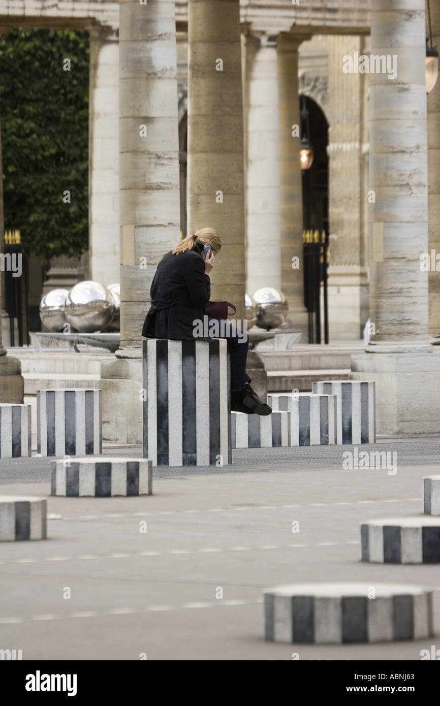 Woman talking on cell phone sits on sculpture column at Palais Royal Paris France Stock Photo