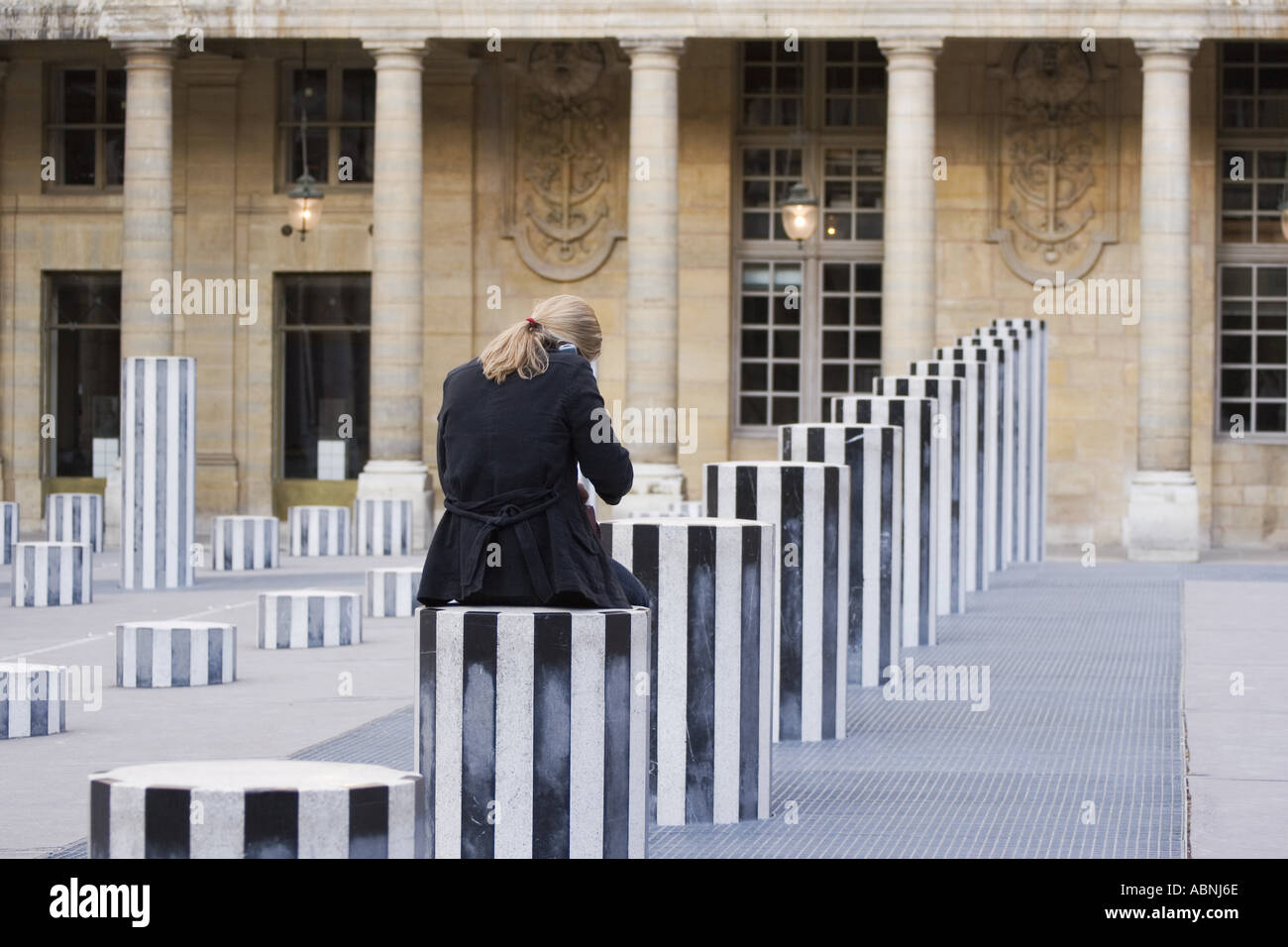 Woman talking on cell phone sits on sculpture column at Palais Royal Paris France Stock Photo