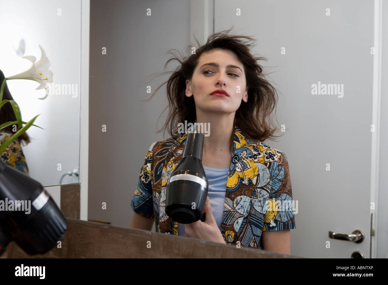 Woman blow-drying her hair in bathroom mirror Stock Photo - Alamy