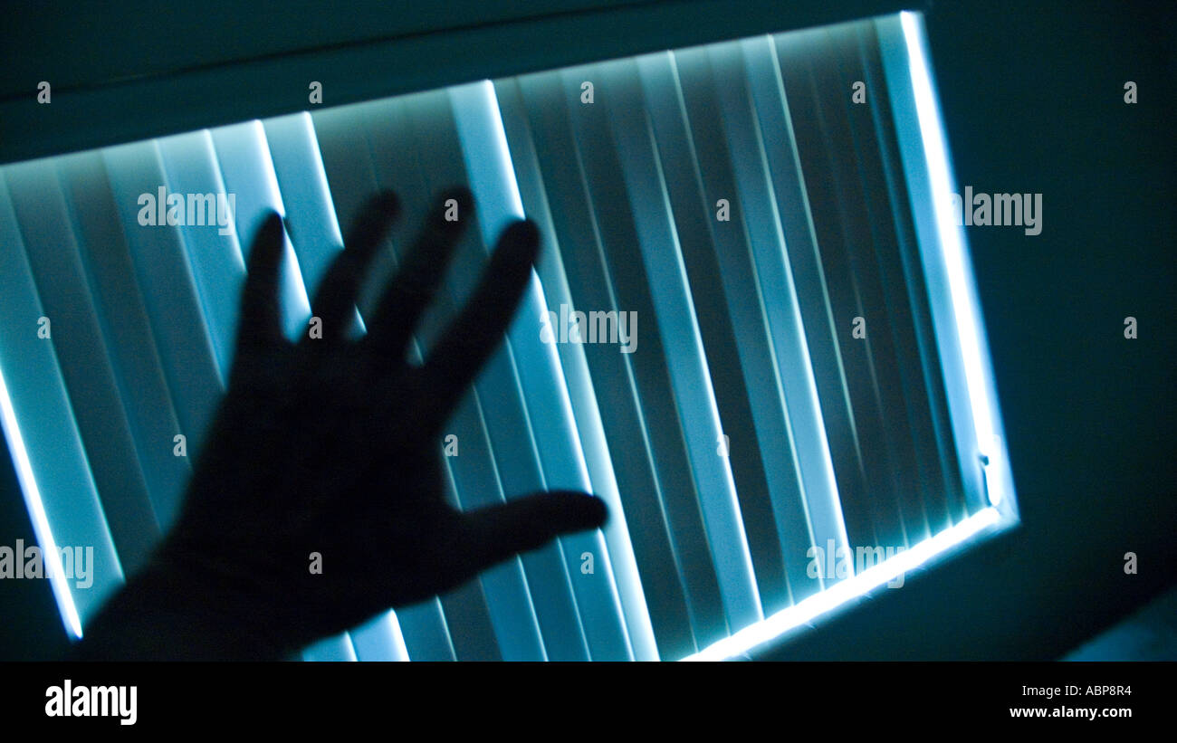 mysterious hand reaching out to venetian blinds Stock Photo