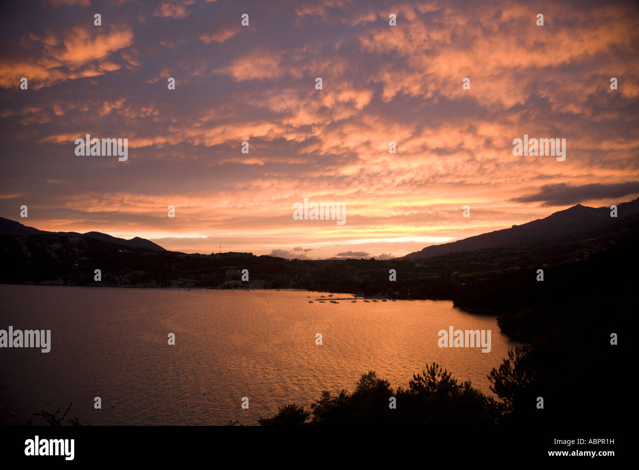 Sunset with bright red coloured clouds over Lake Serre Ponçon, Hautes Alpes, France Stock Photo