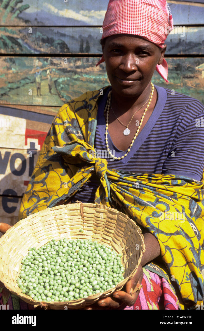 Gitega, Burundi. Woman in the market selling peas and fruit in front of a painted wall with pictures; French words. Stock Photo