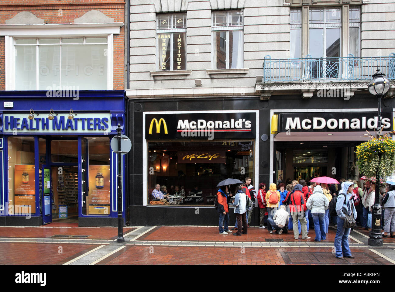 People queueing for Macdonalds burgers next to health food shop Stock Photo