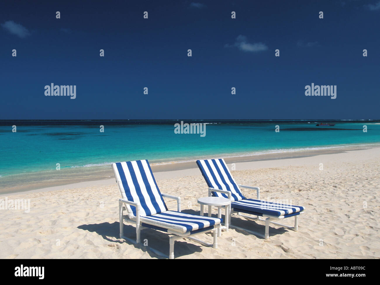 Tropics two cushioned chaise lounges on deserted beach blue green water