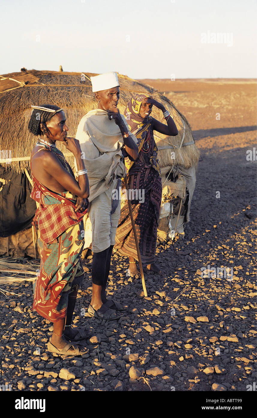 Old Gabbra man with his wife and a younger woman standing outside their hut in the stony desert Stock Photo