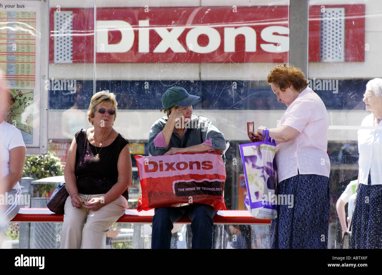 Women shoppers waiting at a bus stop outside a Dixons store Stock Photo
