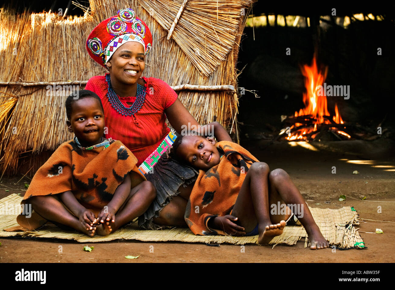 Zulu woman in traditional red headdress married woman with children Beehive hut in background Model released South Africa Stock Photo