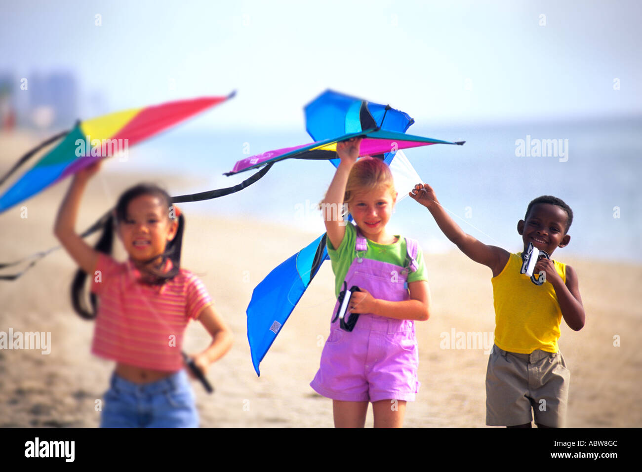 Mixed ethnic children playing on beach flying kites having fun together