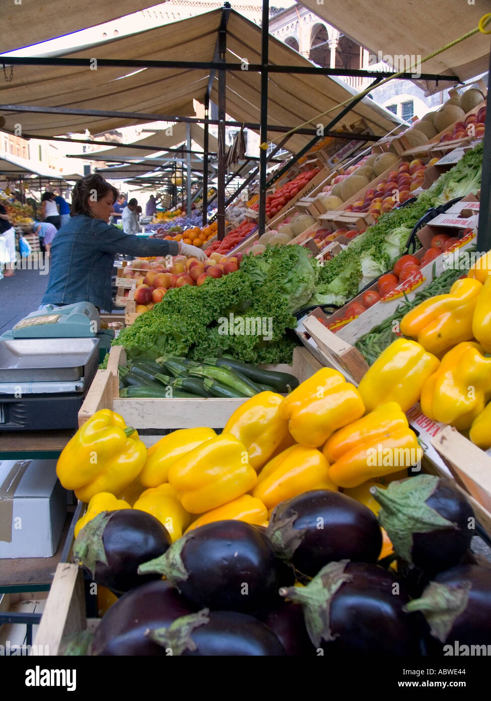 Woman produce vendor arranging fruits and vegetables at market stall in