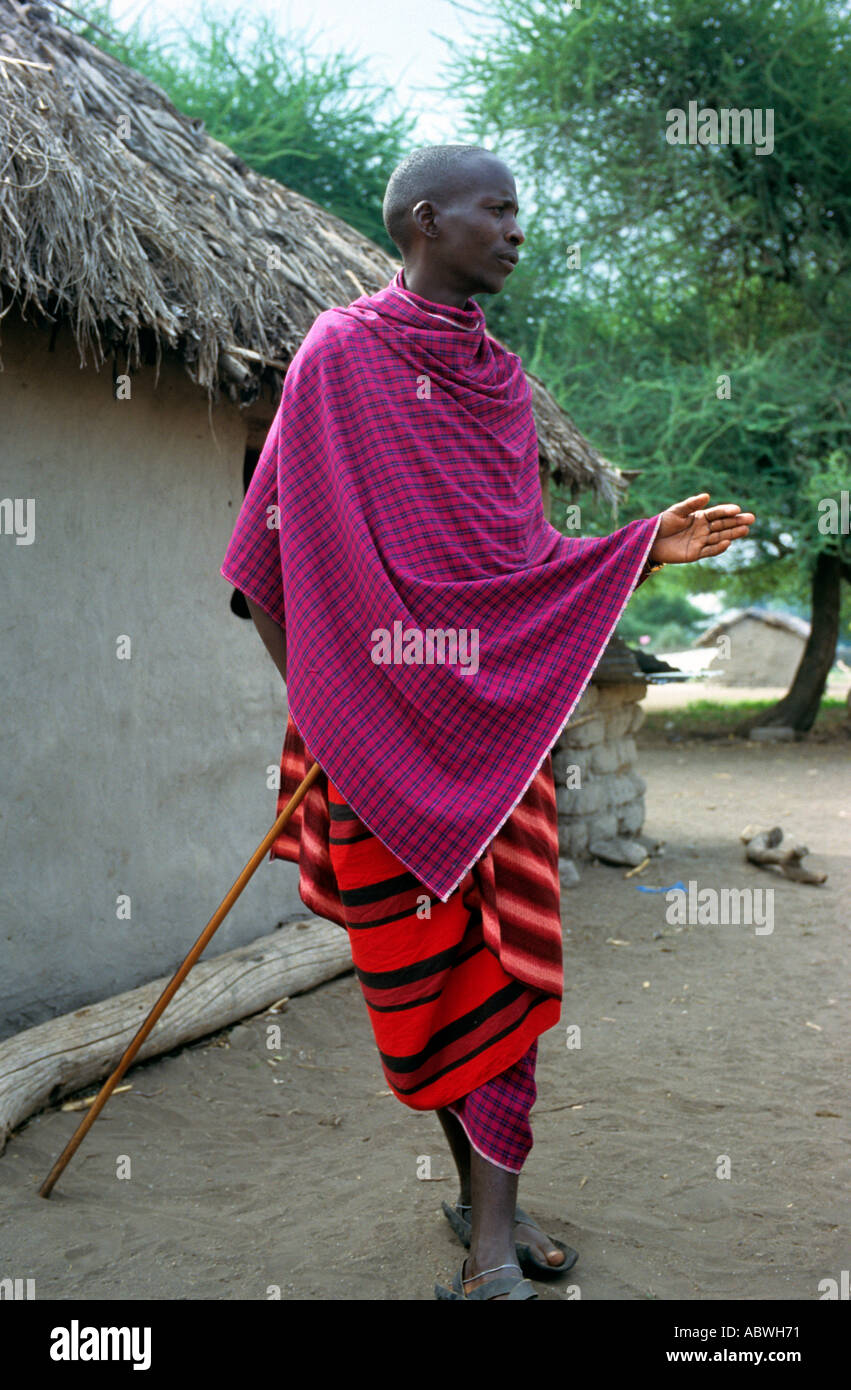 Maasai man dressed in traditional robes outside his home Shambarai