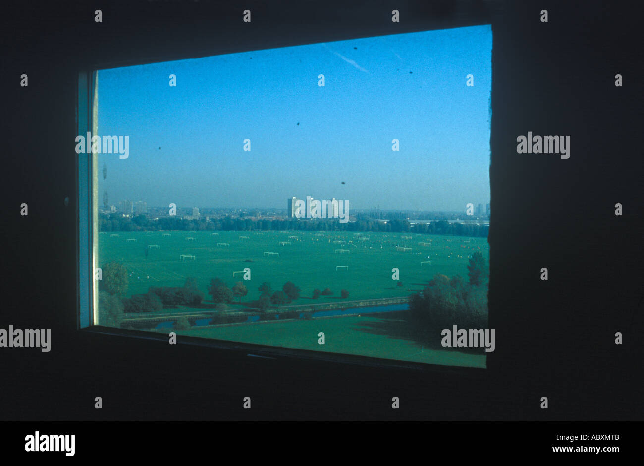 A number of football pitches on Hackney Marshes seen through the fly-covered window of a disused tower block. Stock Photo